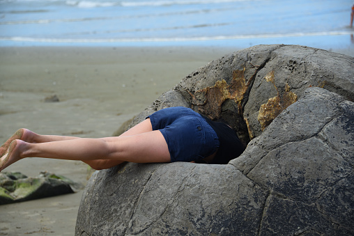 Fun times as a girl tries a head first exploration of the interior of a boulder at the famous Moeraki Boulders in the New Zealand Southland.