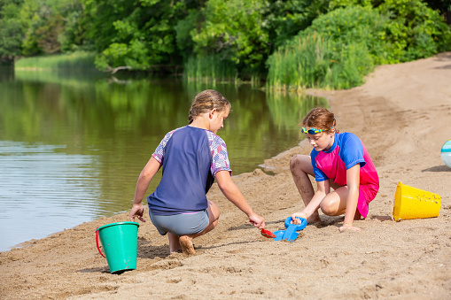 Two young girls (sisters) playing in the sand at the beach on a summer day.