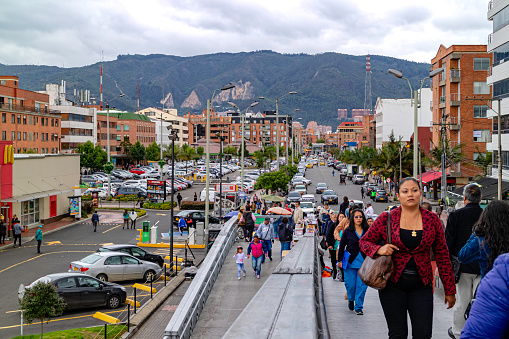 Bogota, Colombia - April 19, 2017: Looking from a footbridge up Calle or Street 125 to the Eastern Hills of the City. To the left is a McDonald's Drive Through outlet on Calle 125. To the right the ramp is packed with people walking to the TransMilenio Rapid Bus Transport station. In the foreground are also some parking lots. The sky is overcast and it will rain fairly soon. The altitude at street level is about 8500 feet above mean sea level. Horizontal format.