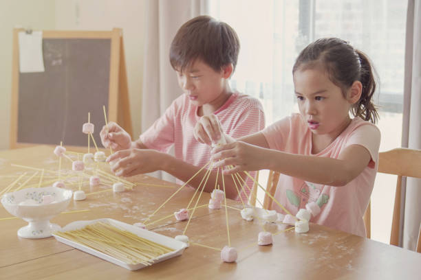 Mixed race young Asian children building tower with spaghetti and marshmallow learning remotely at home, STEM science, homeschooling education, Social distancing, isolation concept