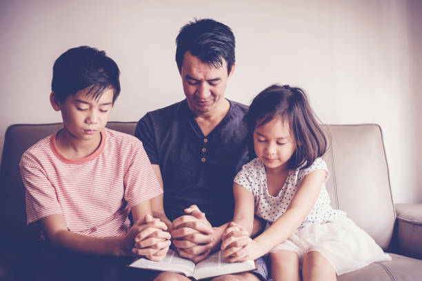 bambini asiatici multiculturali che pregano con il padre a casa, la famiglia prega - family bible foto e immagini stock