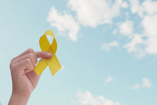 Manos sosteniendo cinta de oro amarillo sobre el cielo azul, Conciencia del Sarcoma, Cáncer óseo, concienciación sobre el cáncer infantil, amarillo de septiembre, concepto del Día Mundial de la Prevención del Suicidio photo