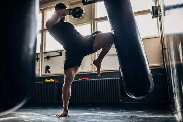 One man, kick boxer training alone in gym, kicking punching bag in gym.