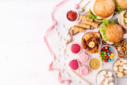 Healthy and unhealthy food concept. Unhealthy food. Sweets and fast food with a measure tape top view om white wooden background