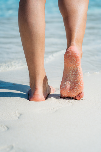 Closeup of woman's feet walking down a tropical sandy beach.