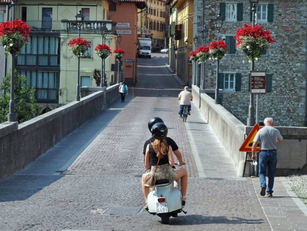 古いヴィンテージベスパと歩行者は、イタリアの町、チヴィデール・デル・フリウリの中心部にある古代の悪魔の橋を渡ります - ベスパ ストックフォトと画像