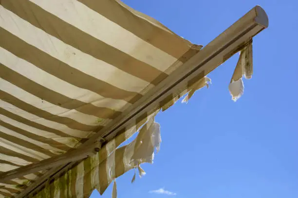 Photo of broken and dirty striped awning in front of azure summer sky