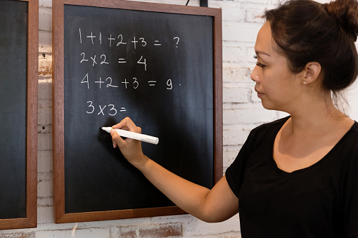 An Indonesian Math teacher writing down mathematical equation for her first grade students.