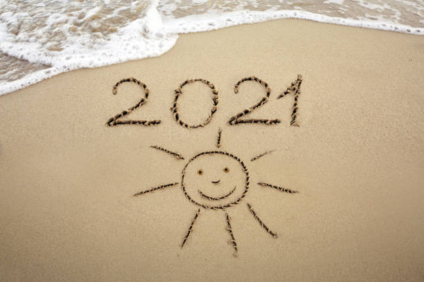 Year 2021 written at the caribbean sand beach with Sun drawing stock photo