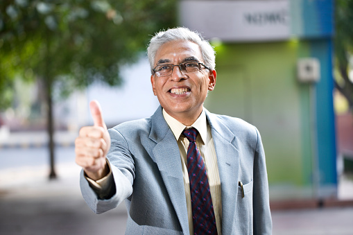 Excited senior businessman giving thumbs up gesture outdoors in city