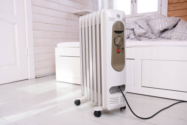 oil-filled electrical mobile radiator heater for home heating and comfort control in the room in a wooden country house - domestic issues imagens e fotografias de stock