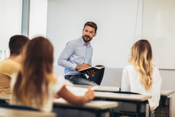 istock Group of smiling students and teacher with notebook in classroom 1252301486