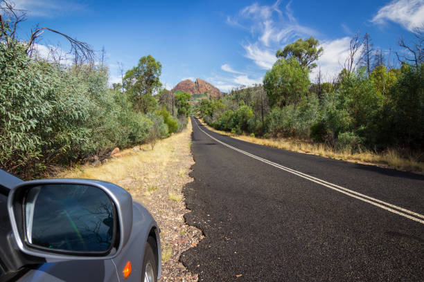 Australian country road trip. Looking out the car window at the road ahead leading to a mountain range. Warrumbungle National Park, NSW, Australia. warrumbungle national park stock pictures, royalty-free photos & images