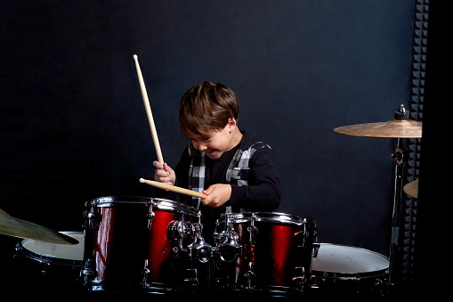 Cheerful smiling child plays the drums. Boys Studios. Dark blue background.