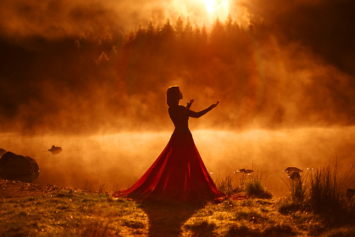 Woman posing in red skirt at the lake during sunset, fog in the background