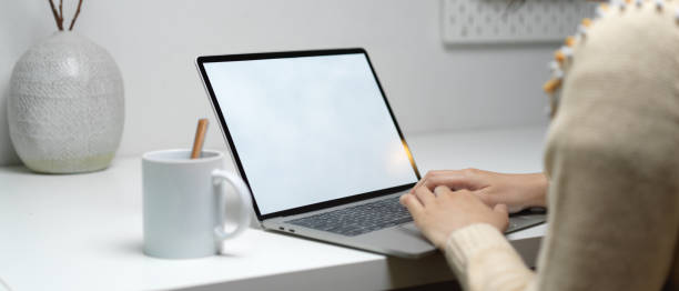 istock Female worker typing on mock-up laptop with coffee mug and ceramic vase on white worktable 1252321078