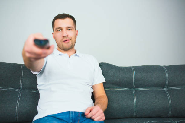 istock Young man sit in room during quarantine. Guy using remote control holding it in one hand. Guy sit alone and switching tv channels. 1252331397