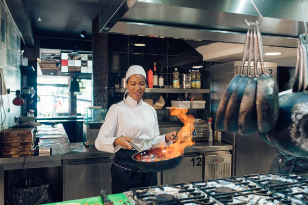 Female chef is preparing a flambé specialty Female chef from the restaurant kitchen is cooking a flambé specialty. chef stock pictures, royalty-free photos & images