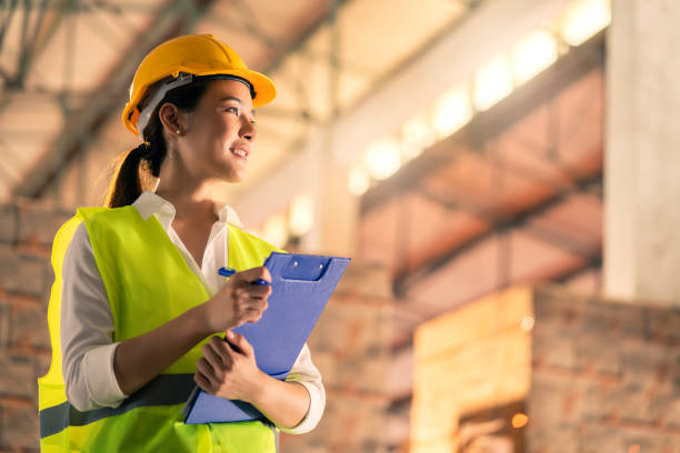 スマートアジアの女性エンジニアの検査官の手の肖像画は、製品在庫のウェアハウスと木製パレットの背景に自信を持って笑顔をチェックする紙チャートの在庫を保持します - construction worker hardhat safety manual worker ストックフォトと画像
