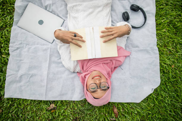 A beautiful young Muslim woman reading the Koran in her living room while standing beside a window