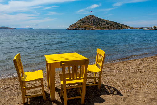 Yellow retro wooden chairs and a table on the beach in Gumusluk, Bodrum