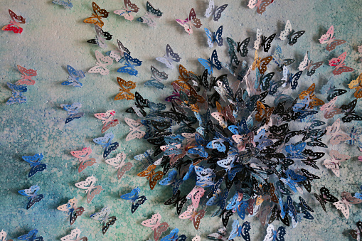 Stock photo showing homemade crafting art work with card and paper butterflies embossed and glued on abstract watercolour painting that has been painted on a stretched canvas. The butterflies were cut out using a butterfly design hole punch.