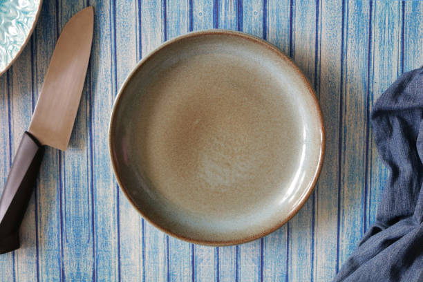 istock Image of group of objects including, mottled brown and blue plate, plain blue tea towel, kitchen knife and blue patterned plate on blue background, blue tongue and groove effect backdrop, elevated view 1252348877