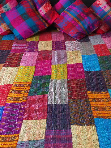 Stock photo showing a bed covered with a brightly, multicoloured patchwork quilt and patterned scatter cushions.