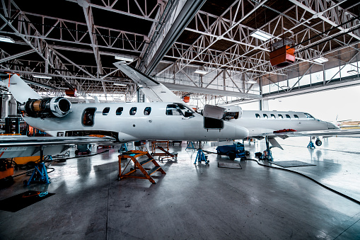Two private jets waiting for maintenance in a repair hangar of an airport.