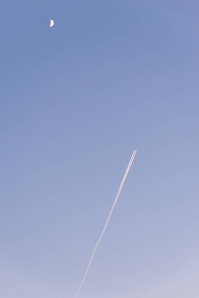 Airplane in the sky with the moon during dusk An aircraft and its condensation trail can be seen in a colourful, wintery sky. contrail moon on a night sky stock pictures, royalty-free photos & images