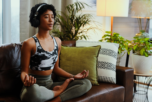 Shot of a young woman listening to music while meditating at home