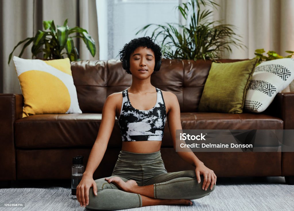 Silence isn't empty - it's full of answers Shot of a young woman listening to music while meditating at home Meditating Stock Photo