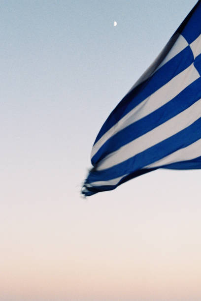 A greek flag can be seen in front of a colourful sky with the moon.