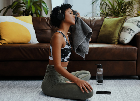 Shot of a young woman wiping her face with a towel while exercising at home