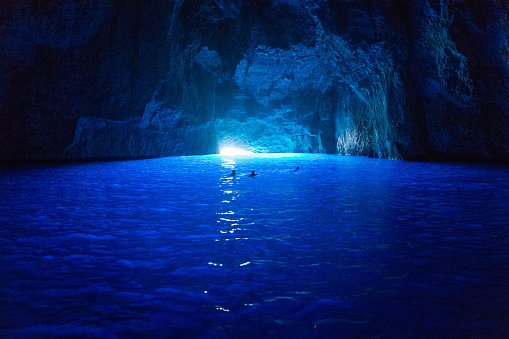People are swimming inside a cave in the Mediterranean Sea that appears blue due to the sunlight entering through the water.