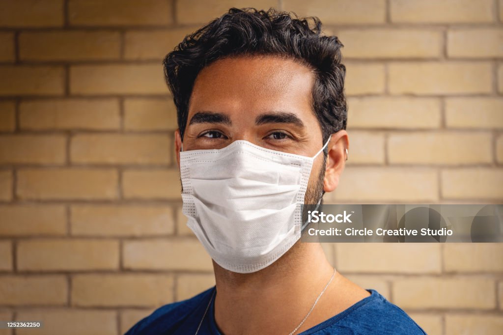 Young man smiling behind the mask during Covid-19 Young man looking at the camera and smiling behind the mask in London during Covid -19 Adult Stock Photo