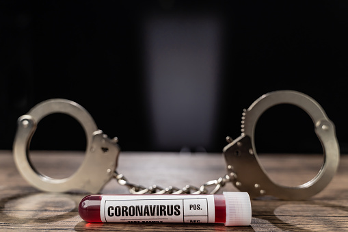 Coronavirus (COVID-19) blood test sample tube and handcuffs on black background. The scene is situated in controlled photography studio environment. Deadliest virus tubes with blood samples in the background. Picture is taken with Sony A7III camera.