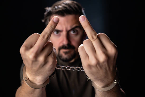 istock Criminal in handcuffs looking at camera and showing middle finger  on black background 1252364654
