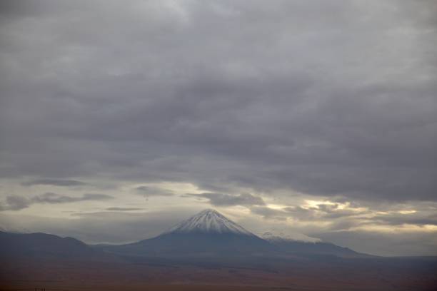 istock volcano with snow on the peak under a dramatic sky and sunbeams sneaking through the clouds. Licancabur, San Pedro de Atacama, Chile 1252366304