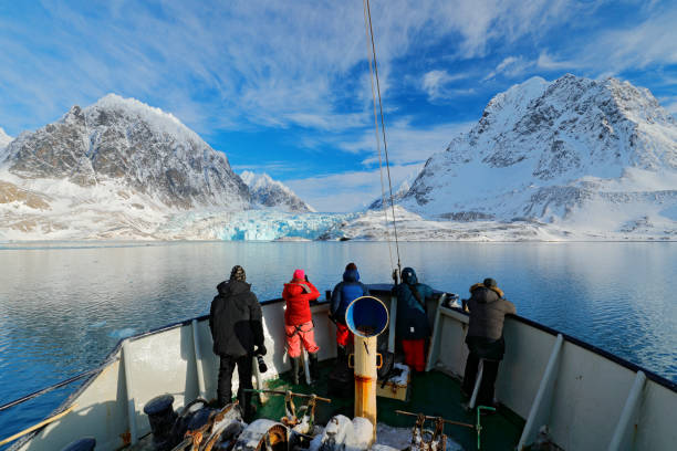 Holiday travel in Arctic, Svalbard, Norway. People on the boat. Winter mountain with snow, blue glacier ice with sea in the foreground. Blue sky with white clouds. Snowy hill in ocean. Travel in sea. stock photo