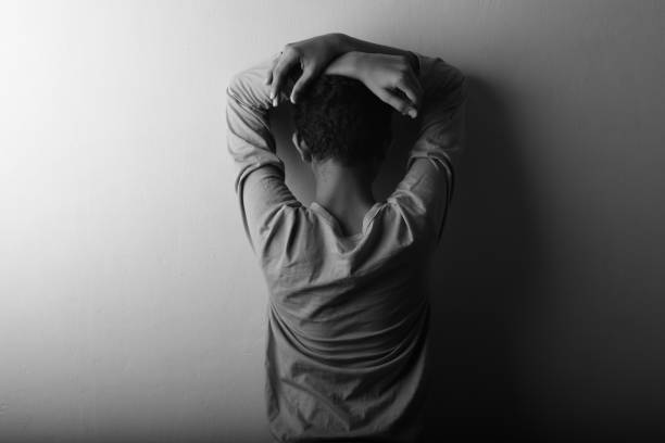 Black and white image of a worried young boy leaning his face on the wall stock photo