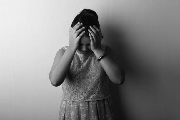 black and white image of a depressed girl placing her hands on head - facial expression child asia asian and indian ethnicities imagens e fotografias de stock