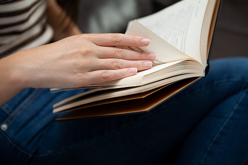 Female hands holding a book resting on her lap