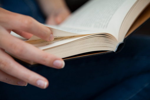 Close up image of A young Asian man reading a book in the garden, selective focus on hand.