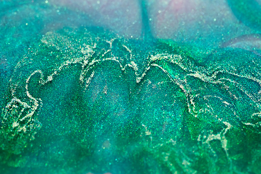 macro shot of green and pink alcohol ink with glitter dissolving in water, beautiful abstract background