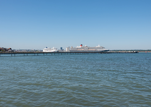 Hythe, UK. Wednesday 35 June 2020. Norwegian Star and MS Queen Victoria in Southampton Docks, with Hythe Pier in the foreground.