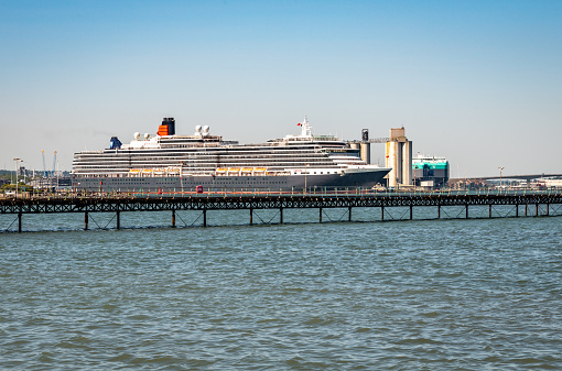 Hythe, UK. Wednesday 35 June 2020. The cruise liner MS Queen Victoria in Southampton Docks in Hampshire with Hythe Pier in the foreground.