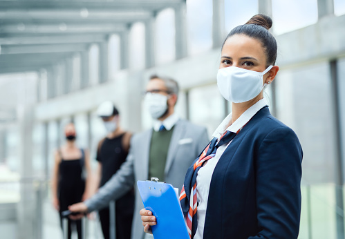 Portrait of flight attendant standing on airport, wearing face masks and looking at camera.