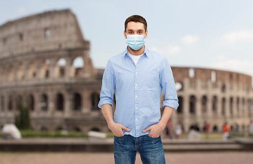 health, safety and pandemic concept - man wearing protective medical mask for protection from virus disease over coliseum in rome, italy background