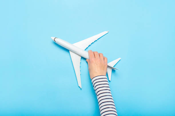 istock Female hand holds a plane on a blue background. Concept flight, tickets, booking, flight search, travel. Banner. Flat lay, top view 1252386784